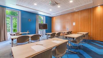 A conference room with multiple tables and chairs, large windows, and a wooden panel wall.