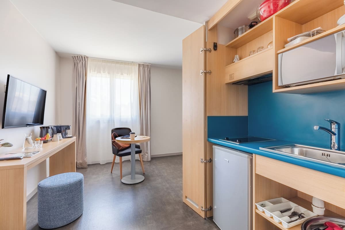 A compact hotel room with a kitchenette, a dining area, and a TV.