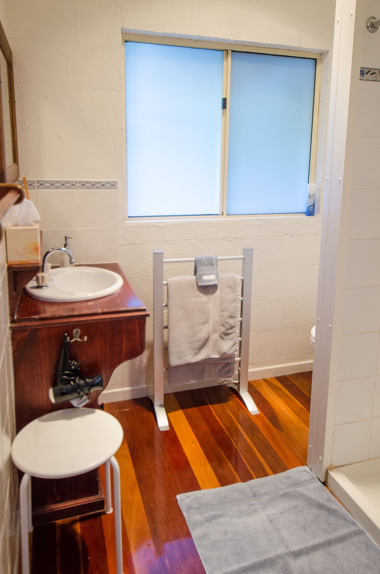 A bathroom with a wooden floor, a sink, a toilet, and a window.