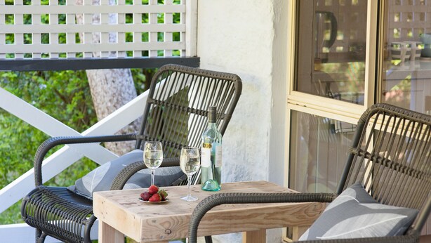 A wooden table with two chairs, two wine glasses, a bottle, and a bowl of strawberries on a porch. - Kidd Street Cottages (Tamborine Mountain)