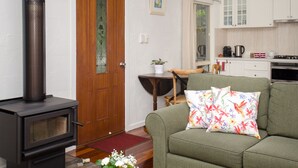 A living room with a fireplace, a sofa with floral cushions, a dining table, and a kitchen in the background. - Kidd Street Cottages (Tamborine Mountain)