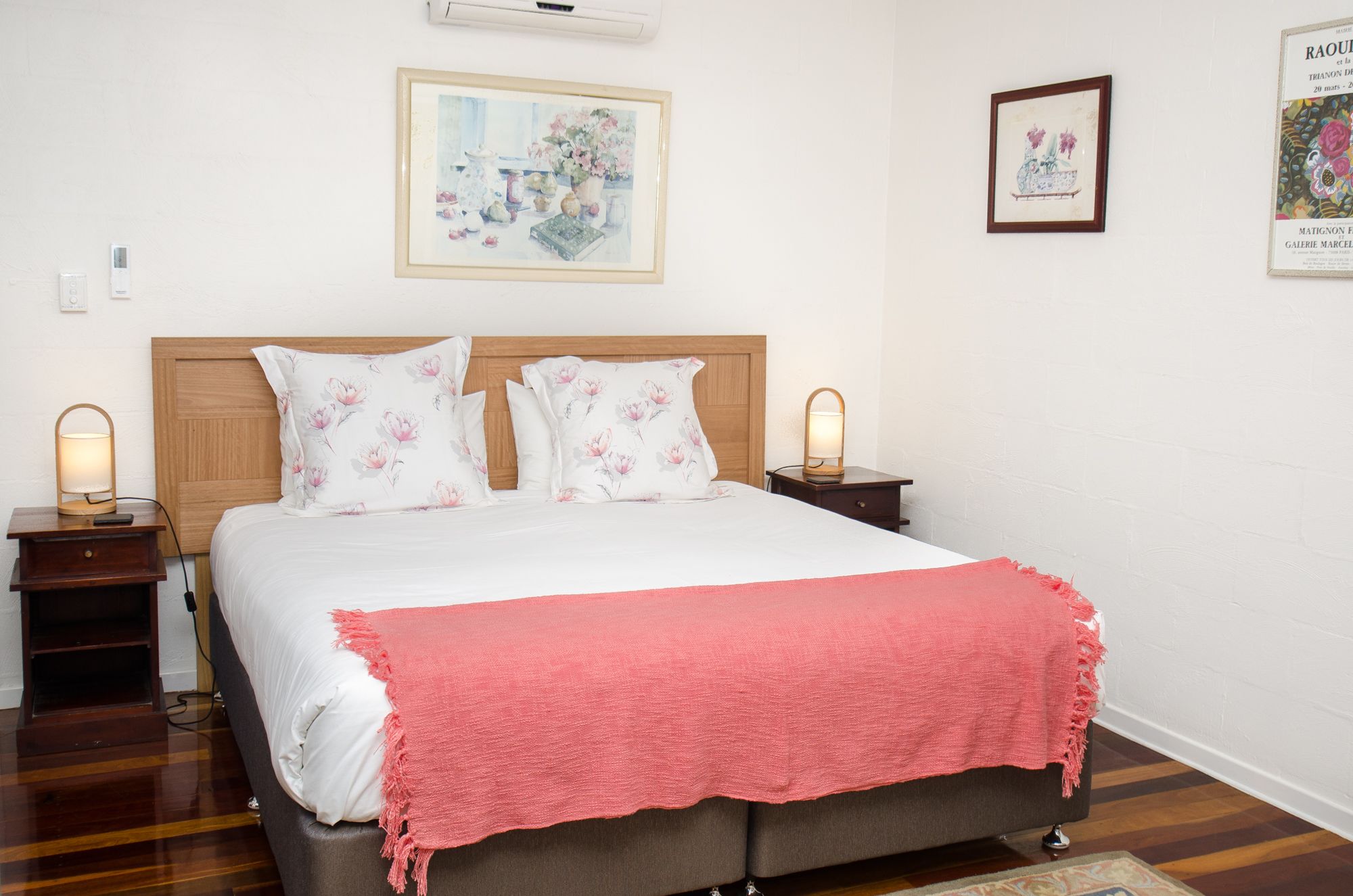 A neatly made bed with floral pillows, a pink throw blanket, and two bedside lamps.
