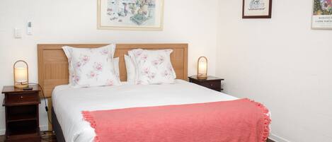 A neatly made bed with floral pillows, a pink throw blanket, and two bedside lamps.