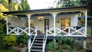 A covered outdoor area with a staircase leading to a door, surrounded by greenery and rocks. - Kidd Street Cottages (Tamborine Mountain)