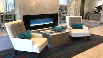 Un salón moderno con un televisor de pantalla plana, dos sillones blancos con cojines turquesa, una mesa de centro y una alfombra estampada.