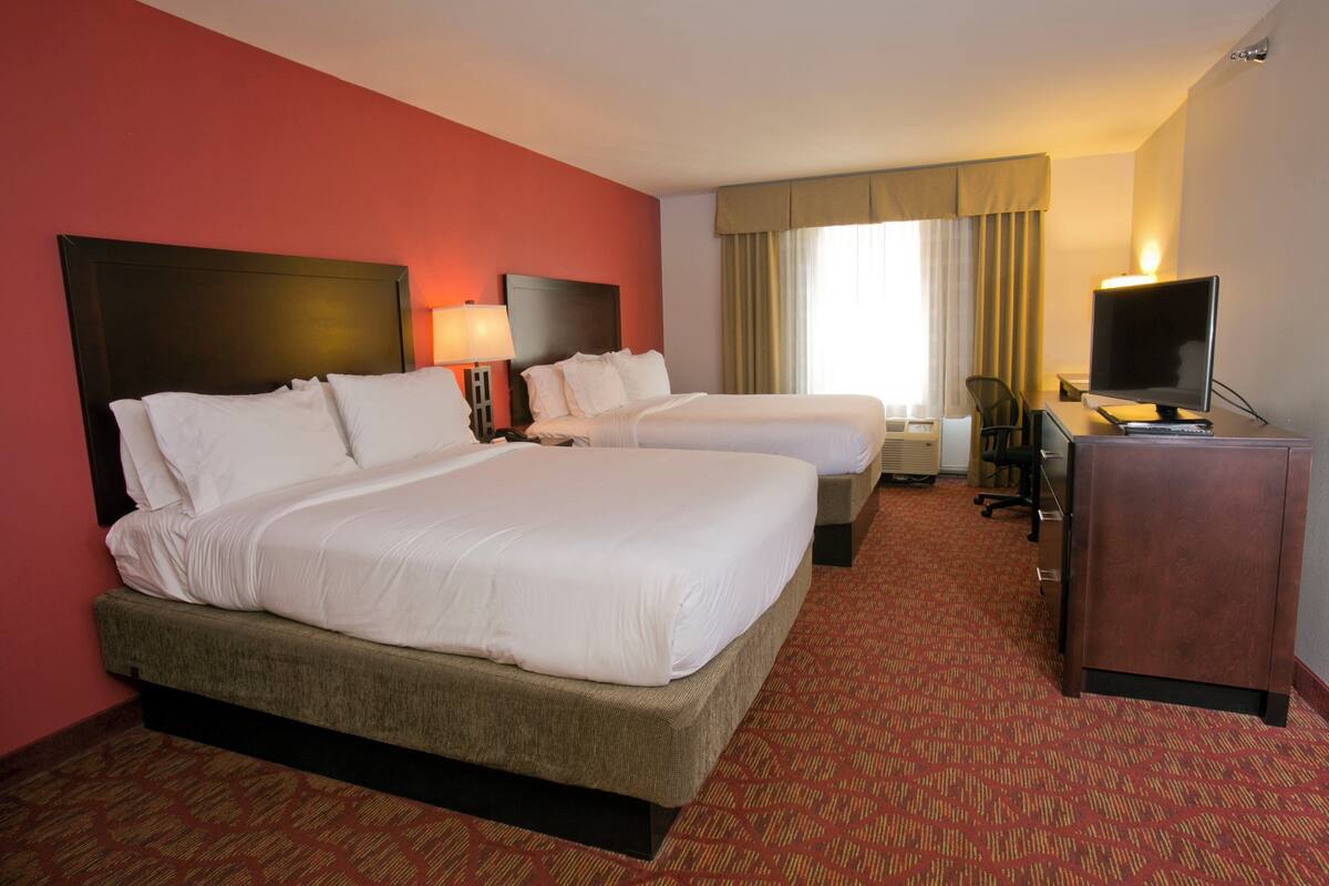 A hotel room with two beds, a desk, a television, and a window with curtains.