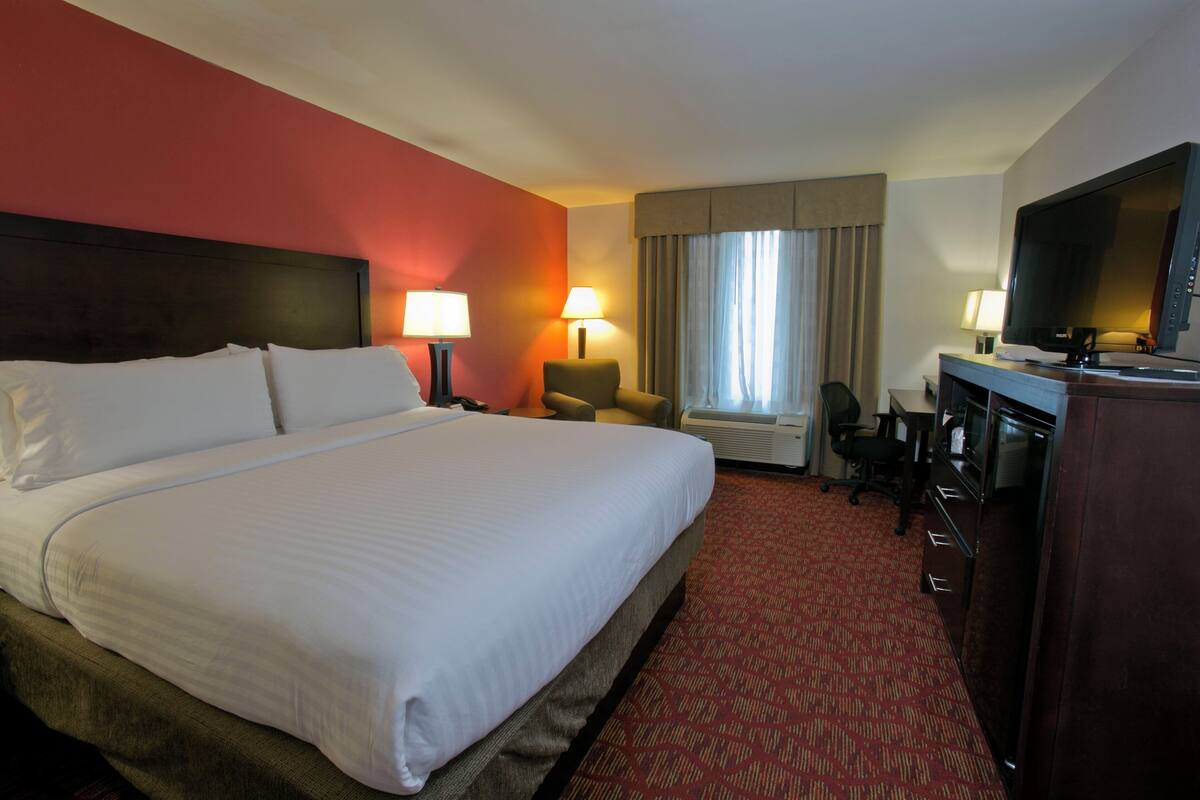 A hotel room with a large bed, two bedside lamps, a desk with a television, and a chair.