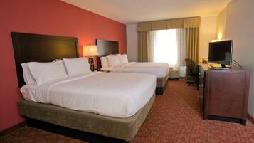 A hotel room with two beds, a desk, a television, and a window with curtains.