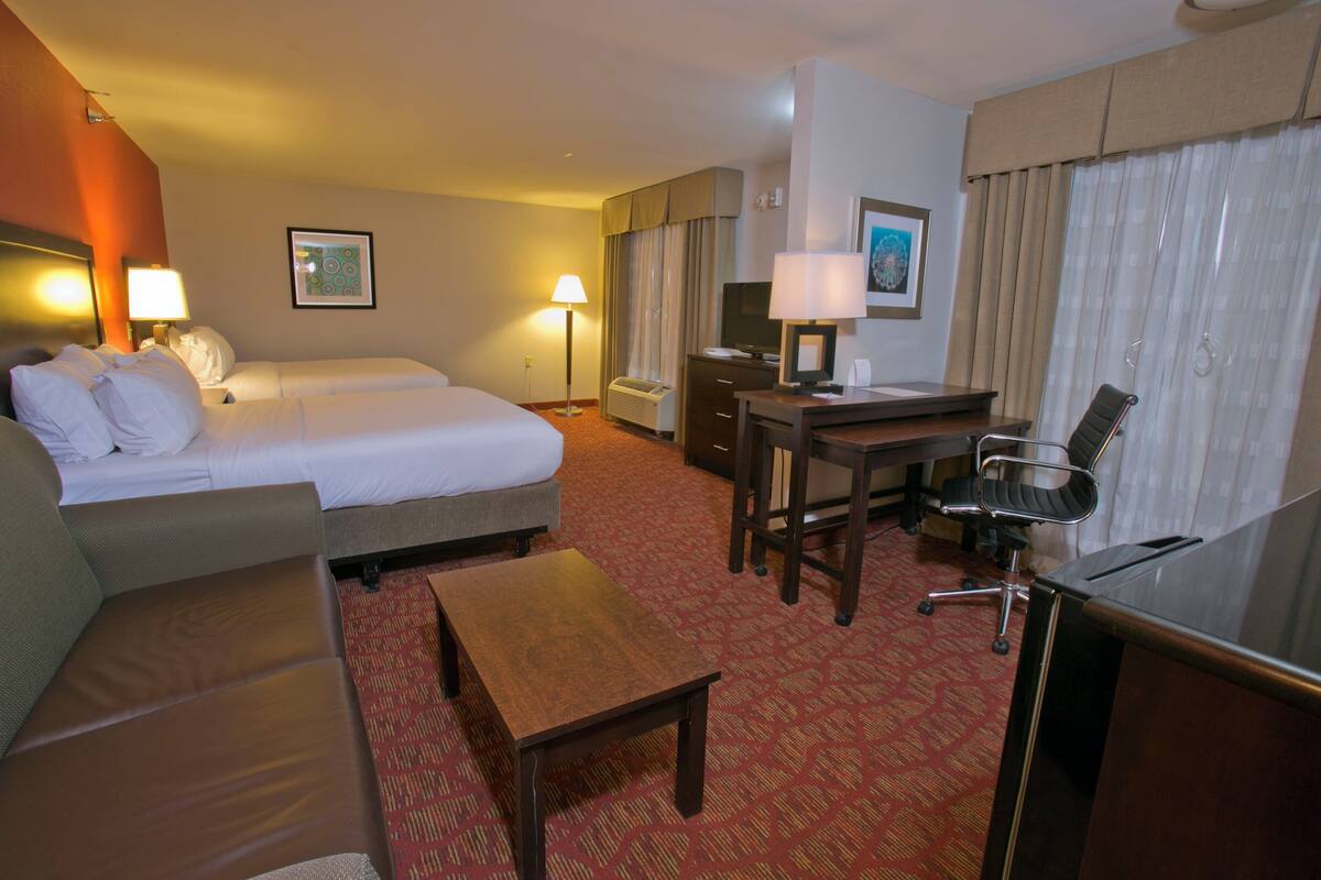 A hotel room with a bed, a sofa, a desk with a chair, and a lamp.
