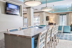 A modern hotel dining area with a large marble island, white chairs, and a television mounted on the wall. - Holiday Inn Express Hotel & Suites Brookhaven by IHG (Brookhaven)