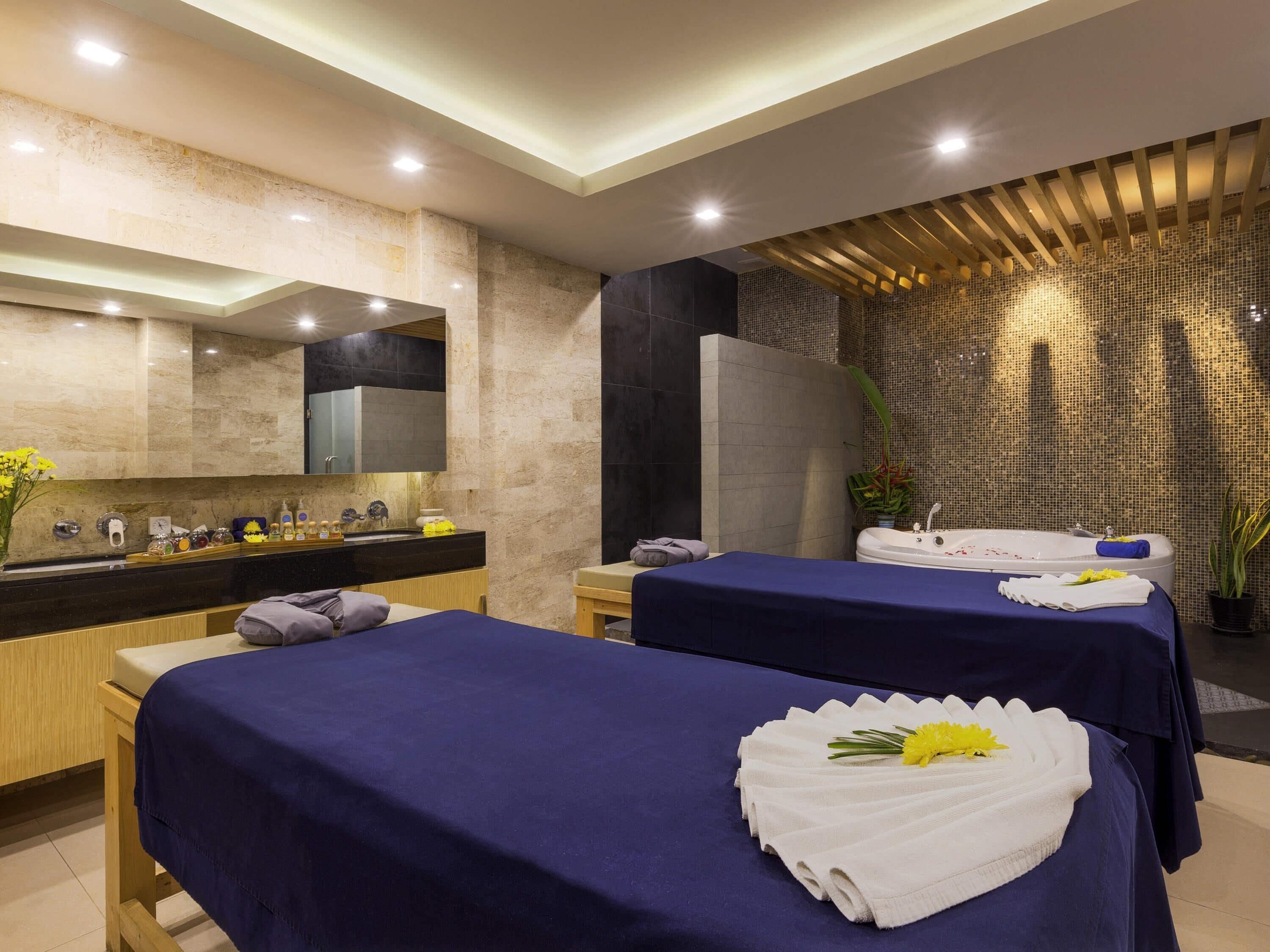 Un moderno spa con dos camillas de masaje, un espejo grande, un lavabo y artículos de aseo, y una decoración en la pared.