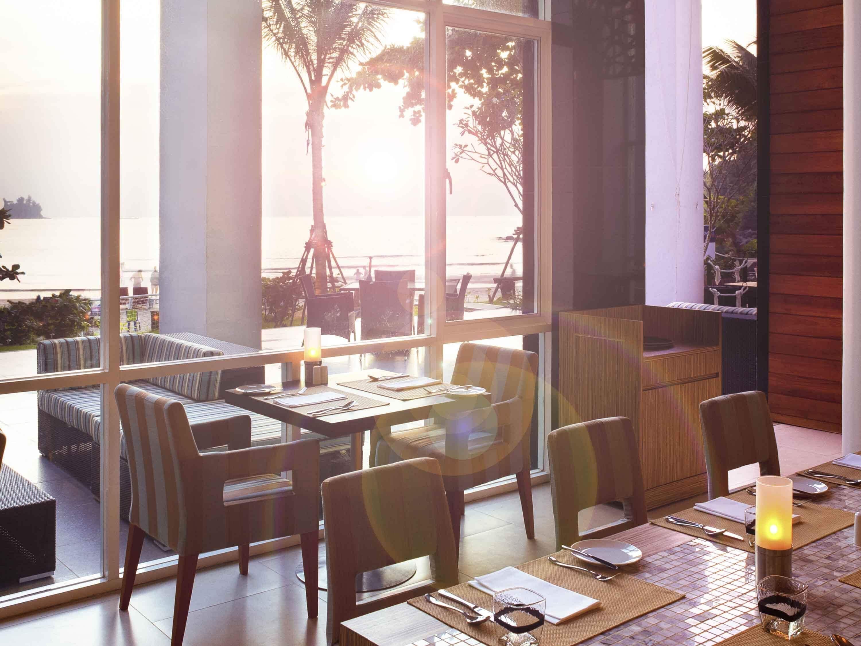 A dining area with tables and chairs, a view of the sea, and a large window.