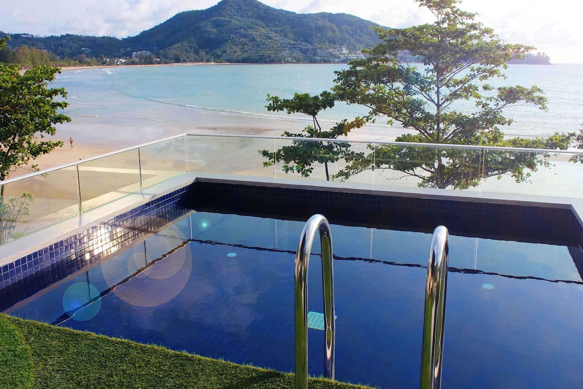 A clear view of a swimming pool with a glass barrier, a beach, and a mountain in the background.