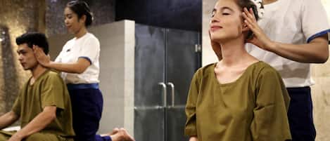Una habitación con una mesa de masajes, una persona recibiendo un masaje en la cabeza y otra persona sentada sobre la mesa.