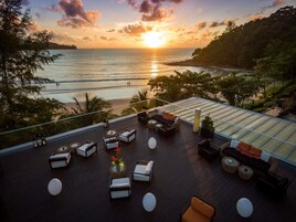 A rooftop terrace with outdoor seating, a glass balustrade, and a view of the sunset over the sea.