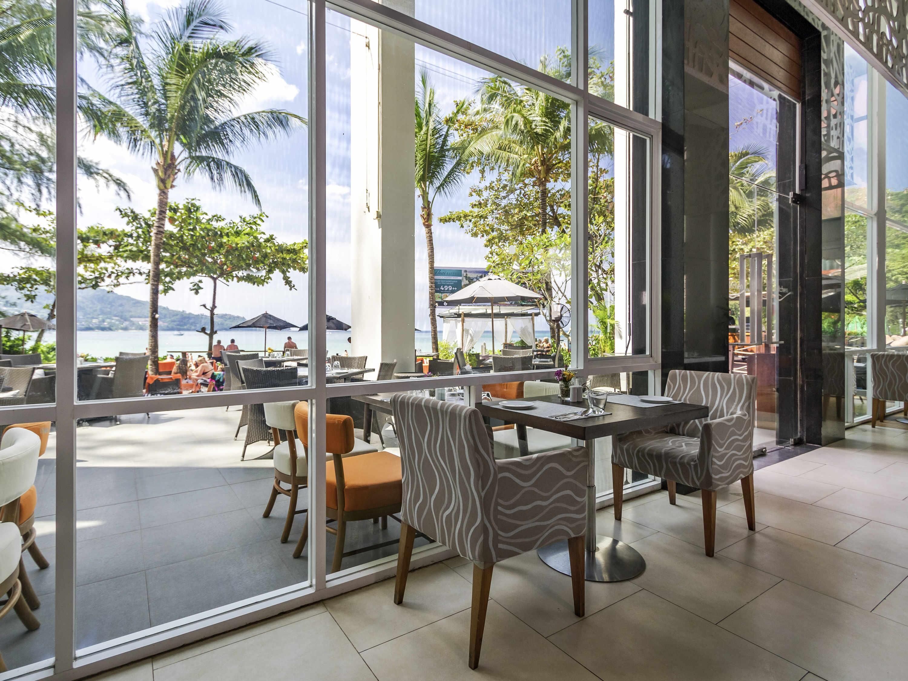 A restaurant with outdoor seating, large windows, and a view of the sea.