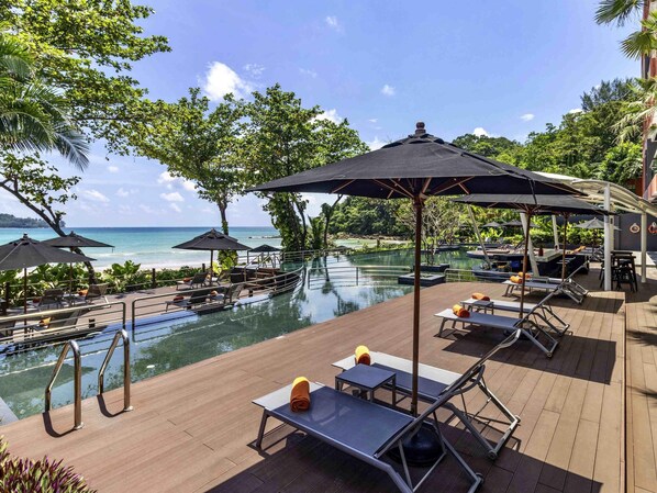 A poolside area with lounge chairs, umbrellas, and a view of the ocean. - Novotel Phuket Kamala Beach (Kamala)