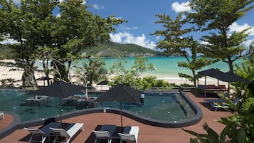 Área da piscina com espreguiçadeiras e guarda-sóis, com vista para uma praia e mar turquesa.