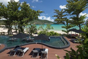 Área da piscina com espreguiçadeiras e guarda-sóis, com vista para uma praia e mar turquesa.