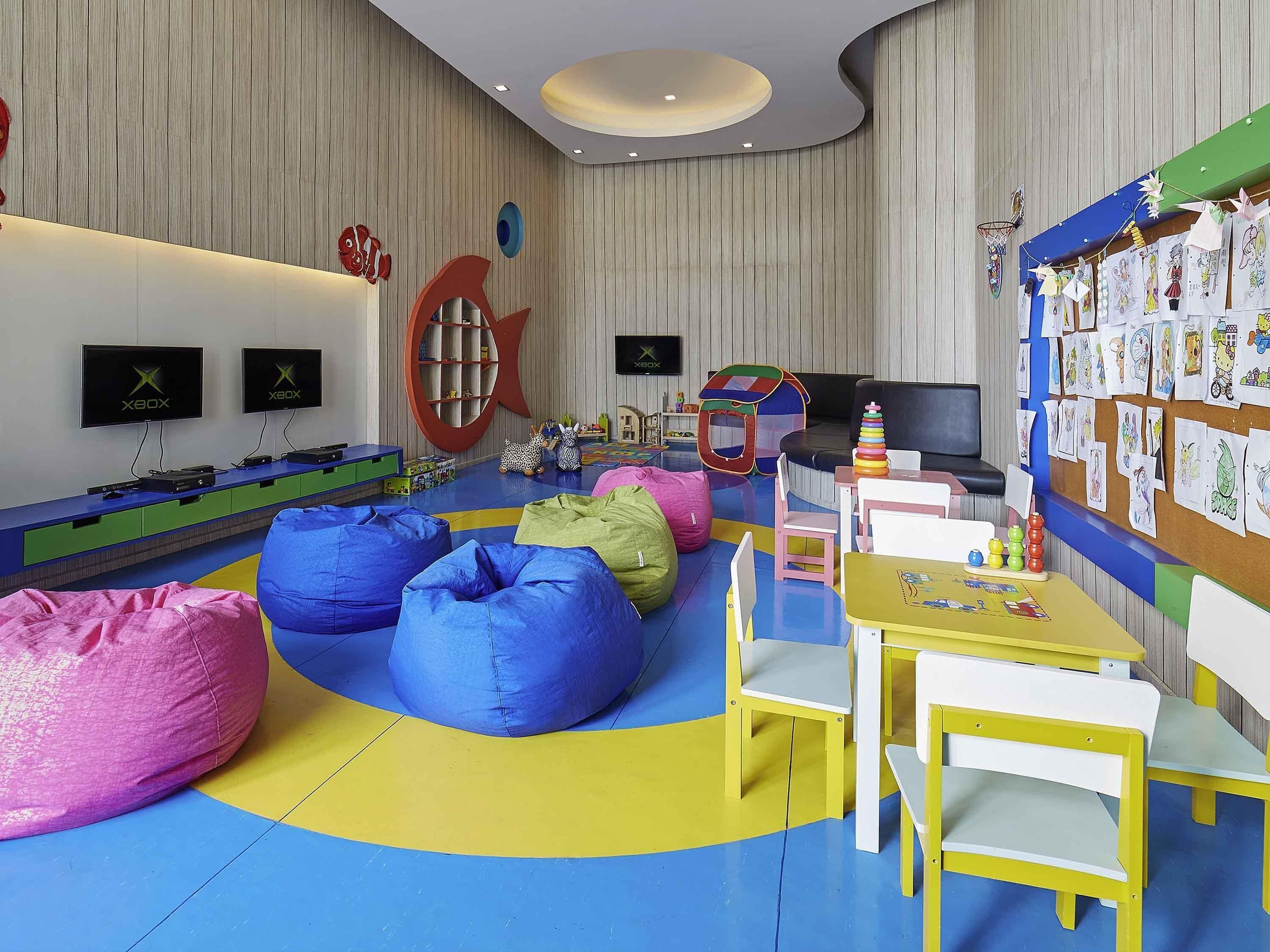 Un área de juegos para niños con pufs, una carpa de juegos y una pared decorada con dibujos infantiles.