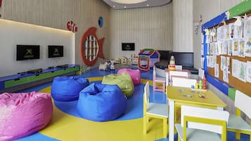 Un área de juegos para niños con pufs, una carpa de juegos y una pared decorada con dibujos infantiles.