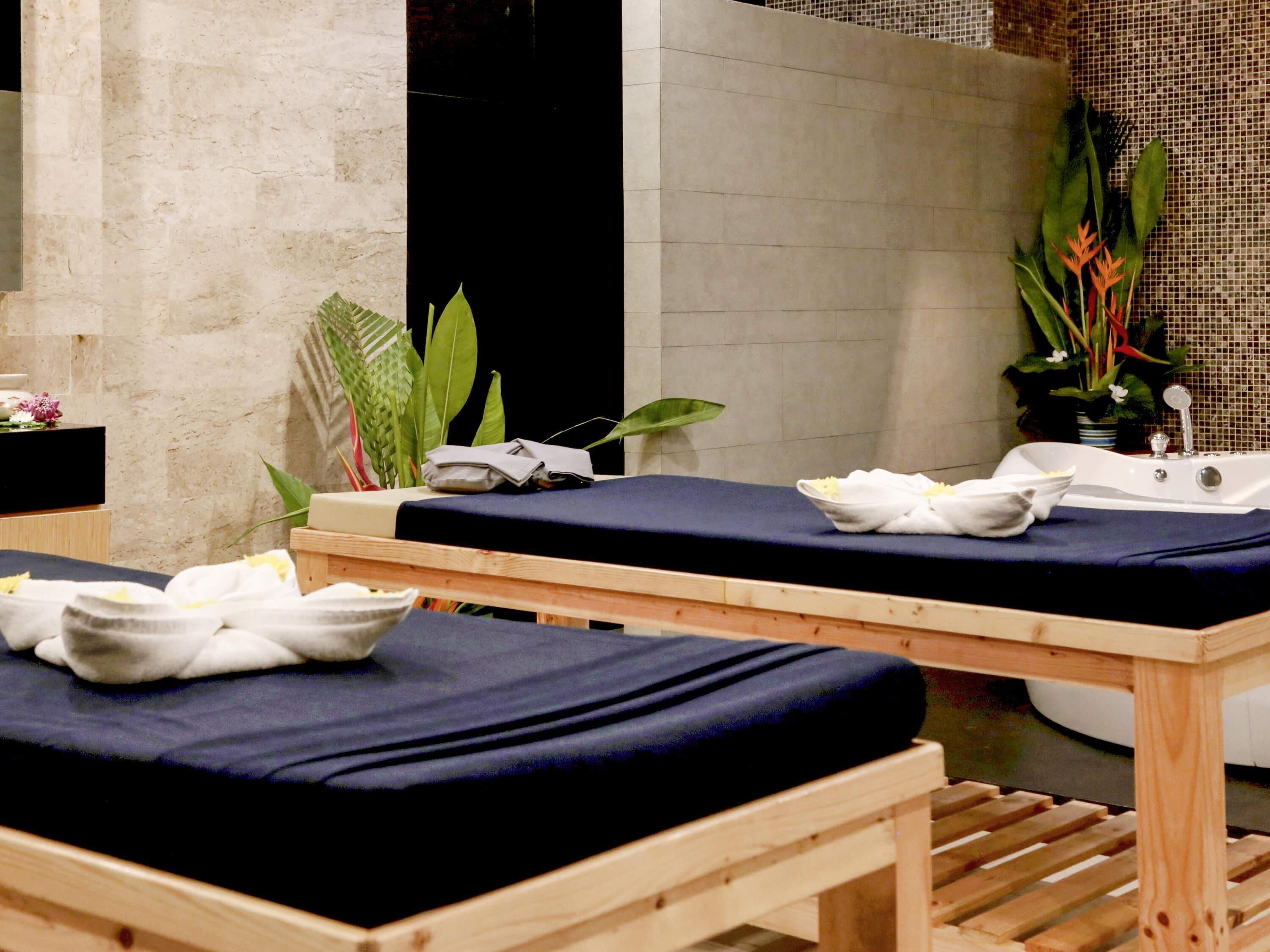 A spa room with two massage tables, a bathtub, and various plants.