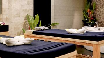 A spa room with two massage tables, a bathtub, and various plants.