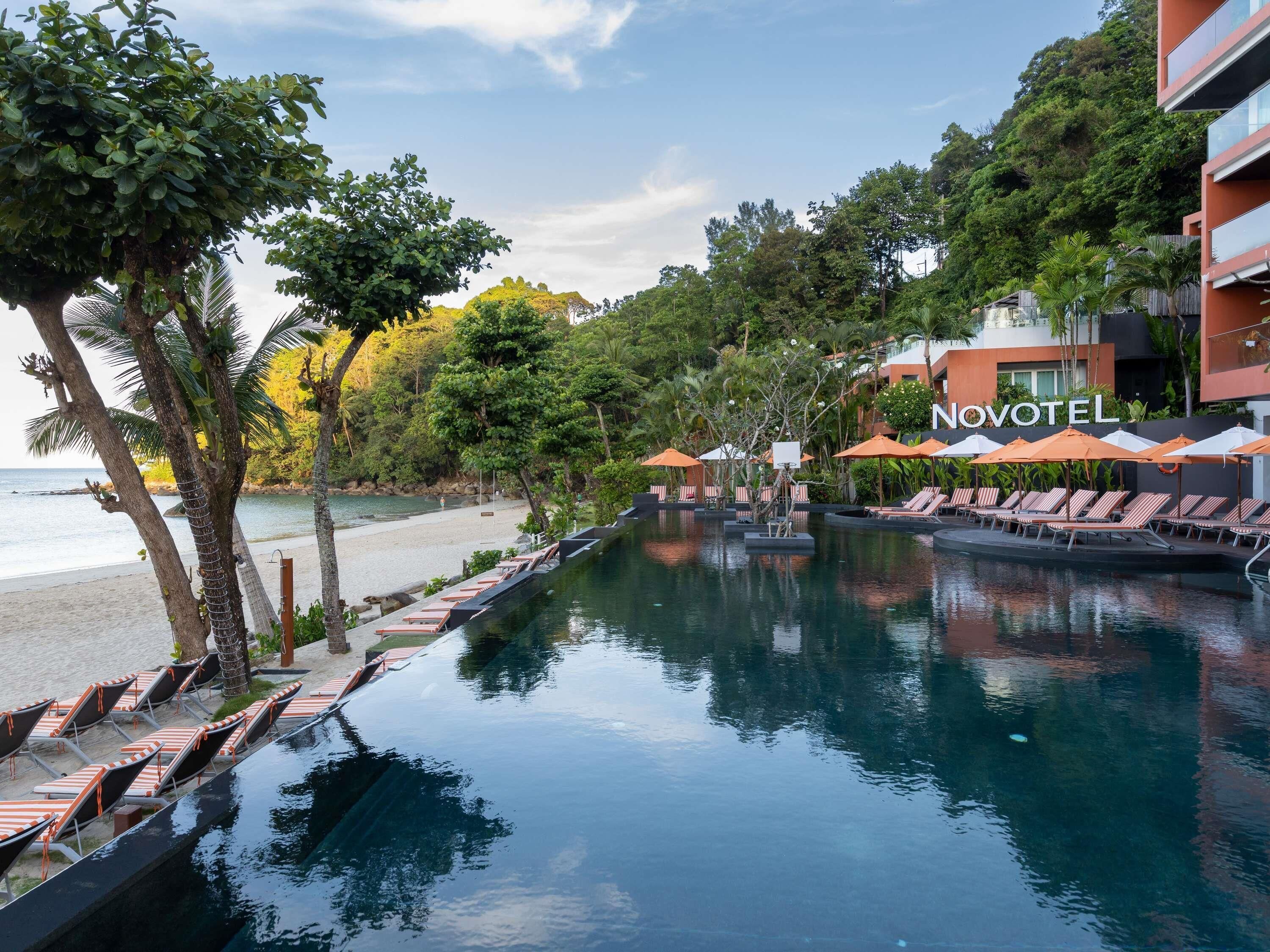 A pool area with lounge chairs, umbrellas, and a sign for Novotel.