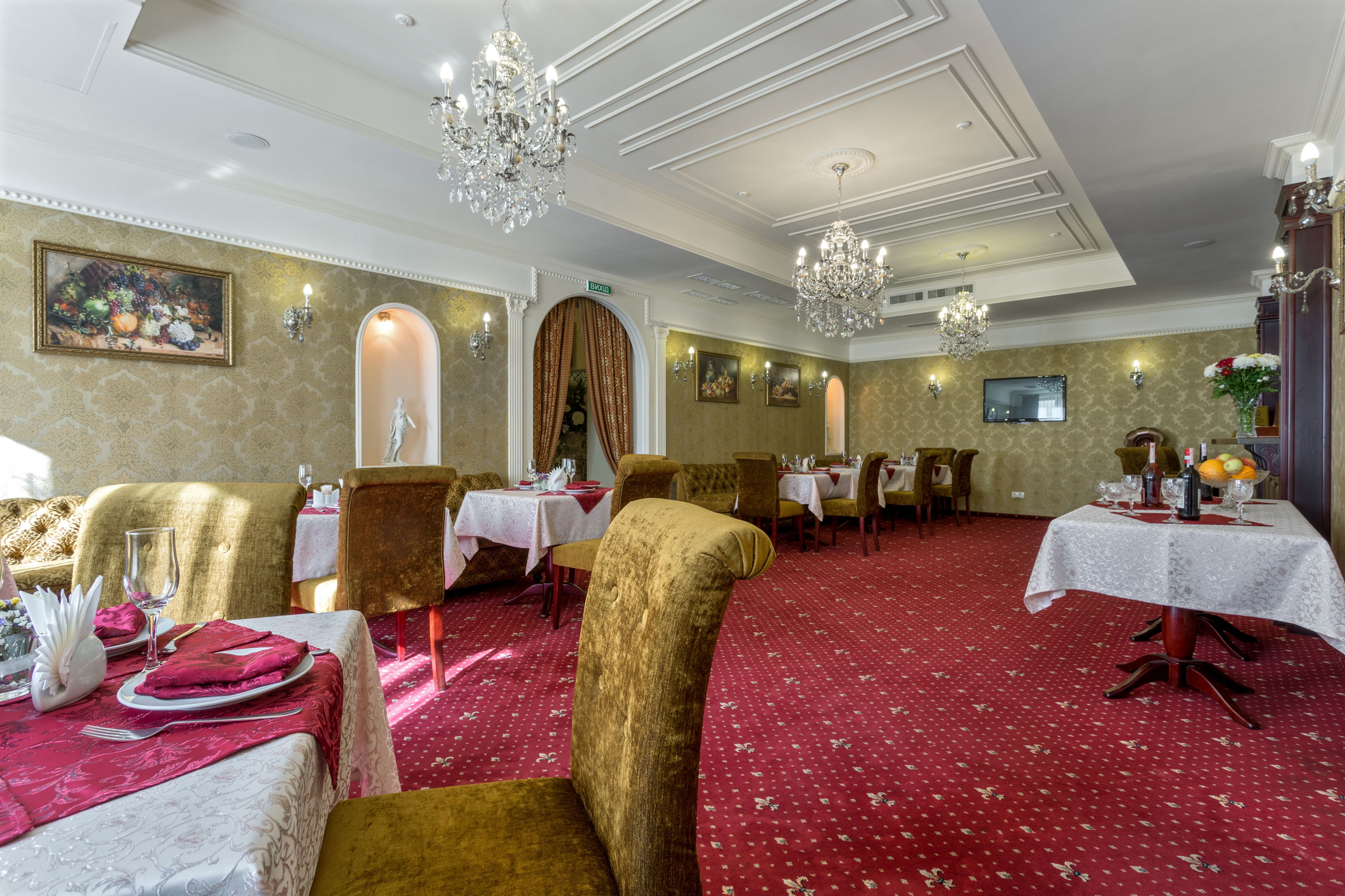 A formal dining room with gold chairs, red carpet, and chandeliers.