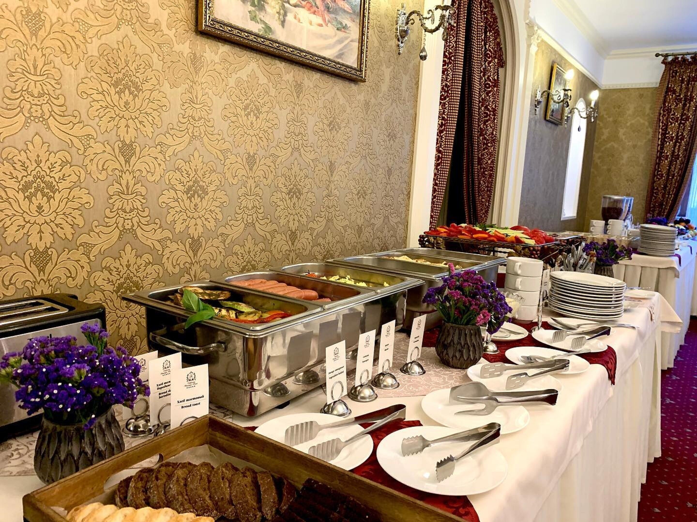 Montaje tipo bufé con diversos alimentos, como carnes, frutas y pan, dispuesto sobre una mesa con platos, cubiertos y un florero.