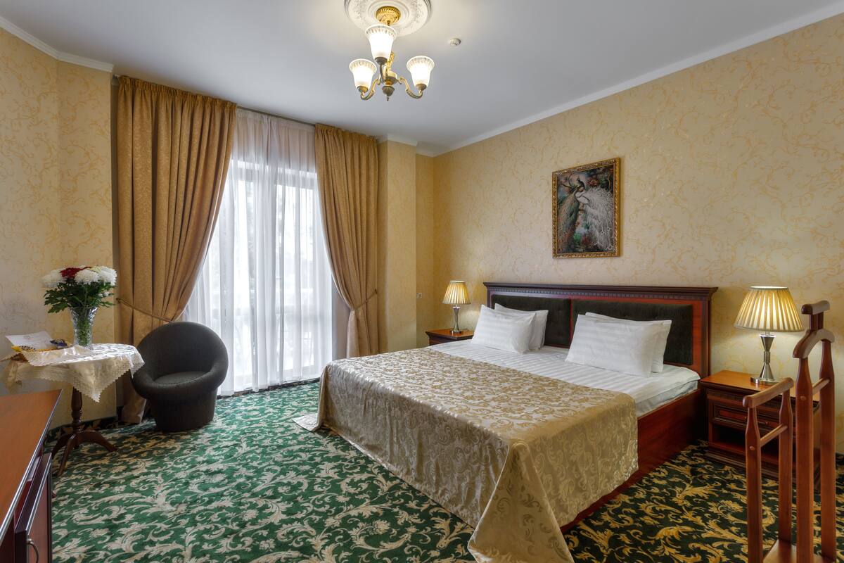 Hotellihuone, jossa on suuri sänky, tuoli, työpöytä ja ikkuna, jossa on verhot.