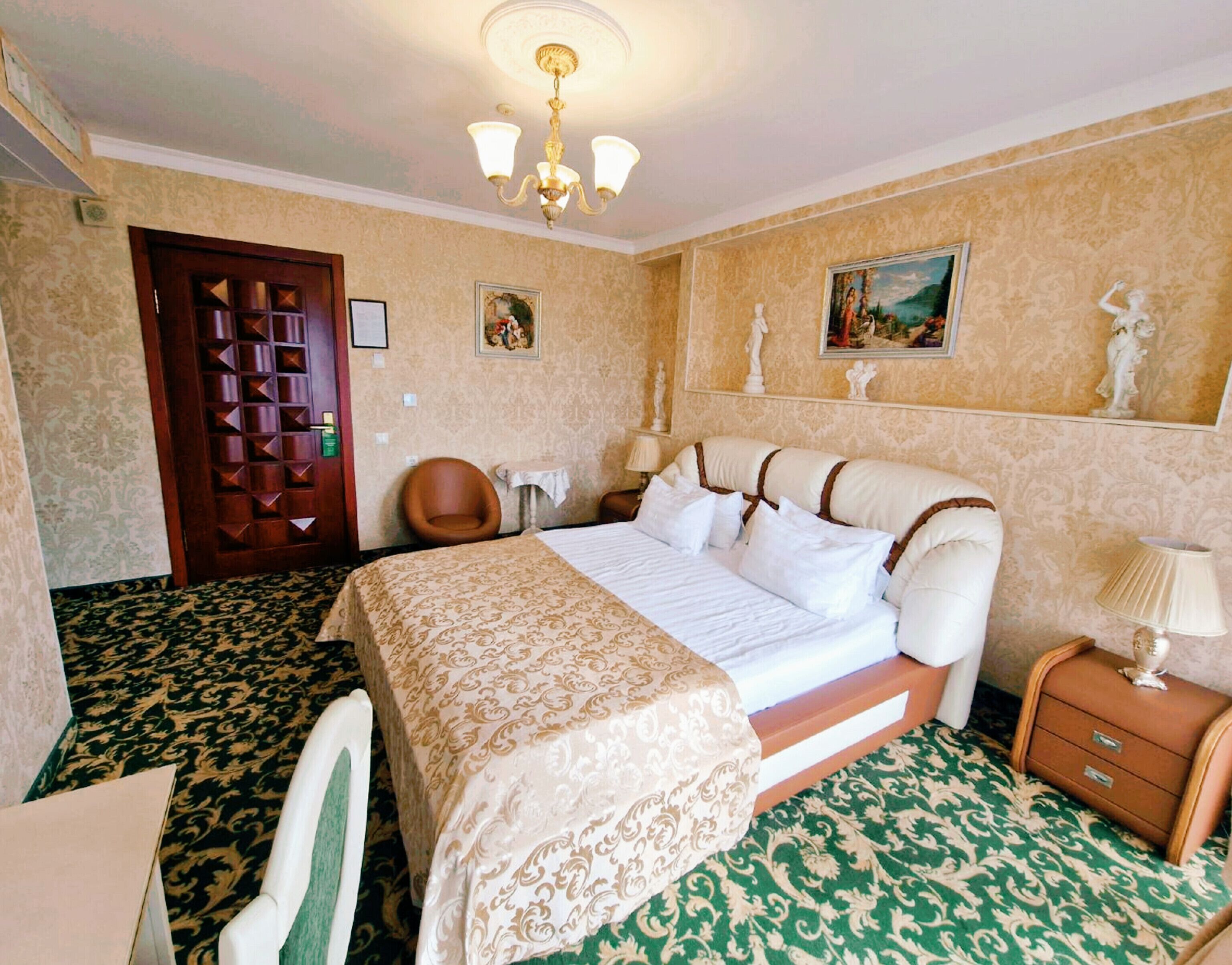 Habitación de hotel con cama, una silla, una mesita de noche, lámpara y puerta.