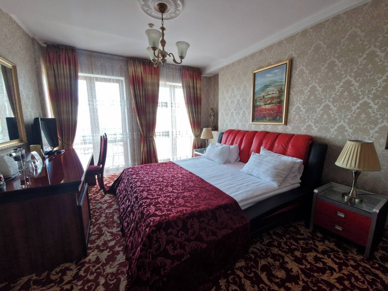 Ein Hotelzimmer mit einem großen Bett, einem Schreibtisch mit Stuhl, einer Lampe und einem Bild an der Wand.