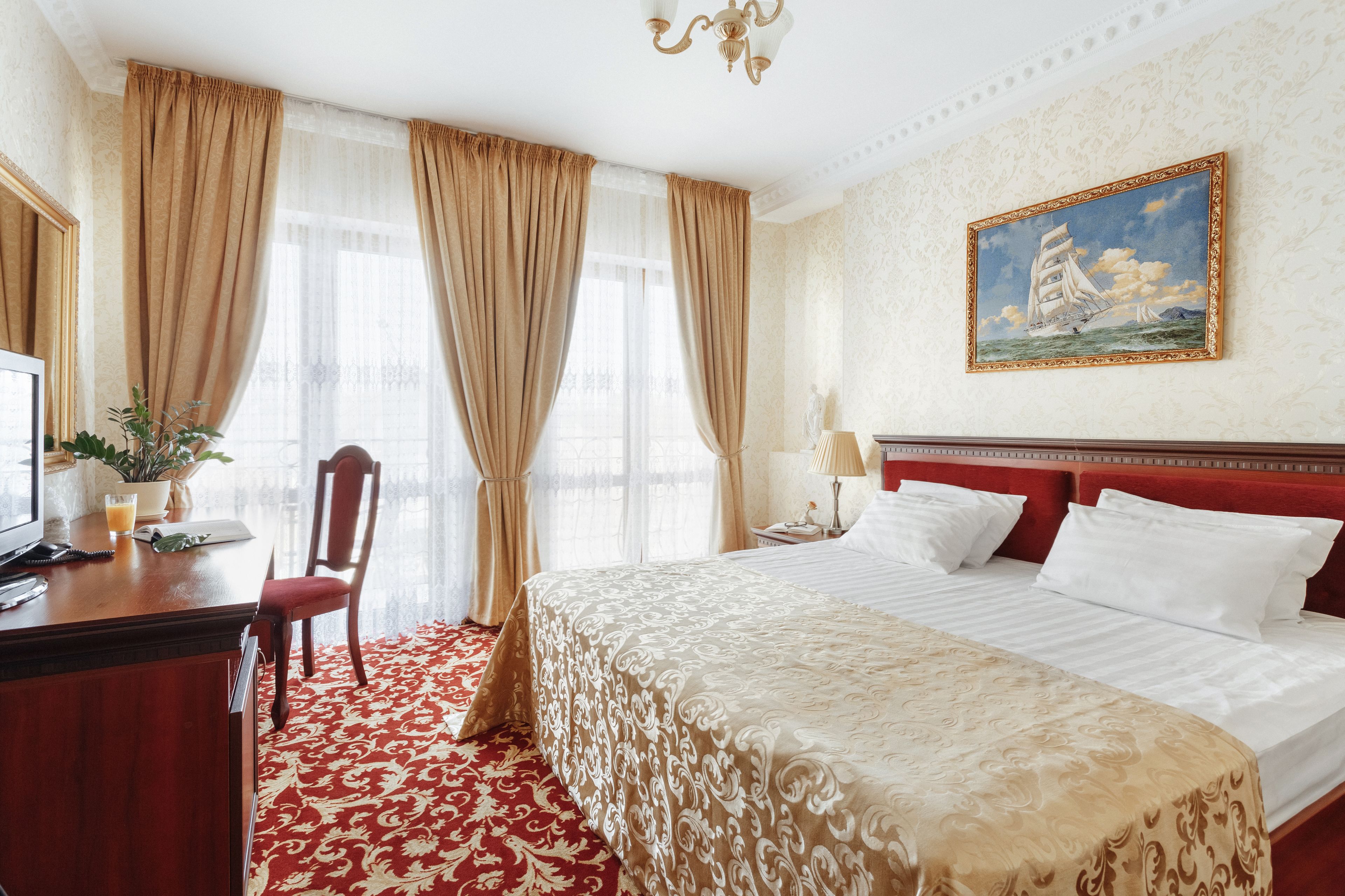 A hotel room with a large bed, a desk with a telephone and a plant, and a painting on the wall.