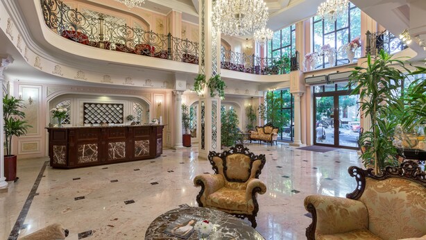 Un amplio vestíbulo con piso de mármol, muebles ornamentados y un techo alto con candelabros.