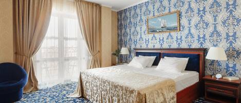 A hotel room with a large bed, a nightstand, a chair, and a window with curtains.