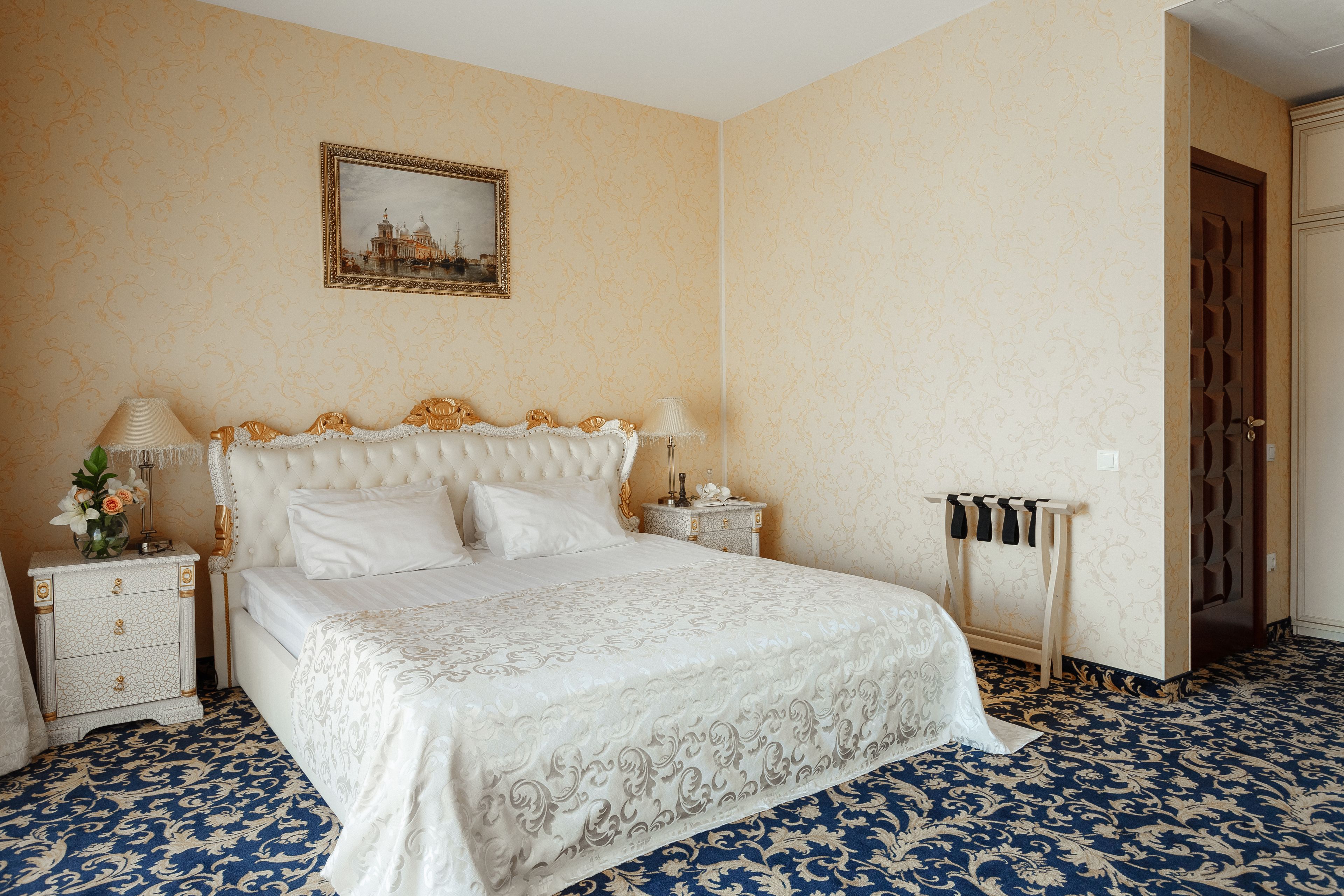 A bedroom with a large bed, a nightstand, a bedside table, and a wall-mounted picture.