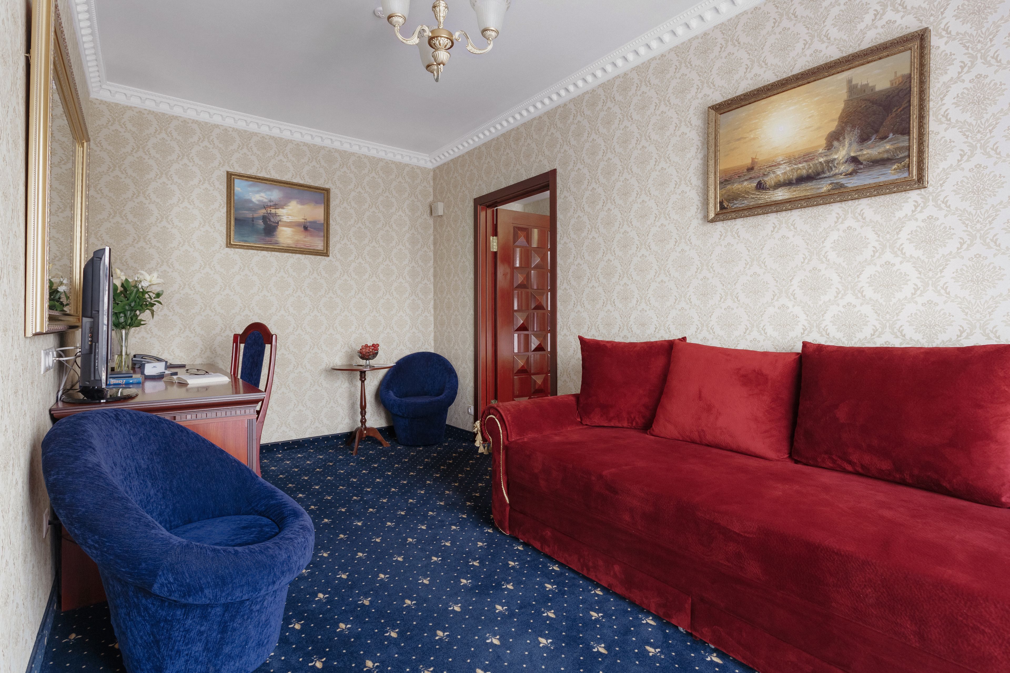 A room with a red sofa, a blue armchair, a small table with a vase, and a painting on the wall.