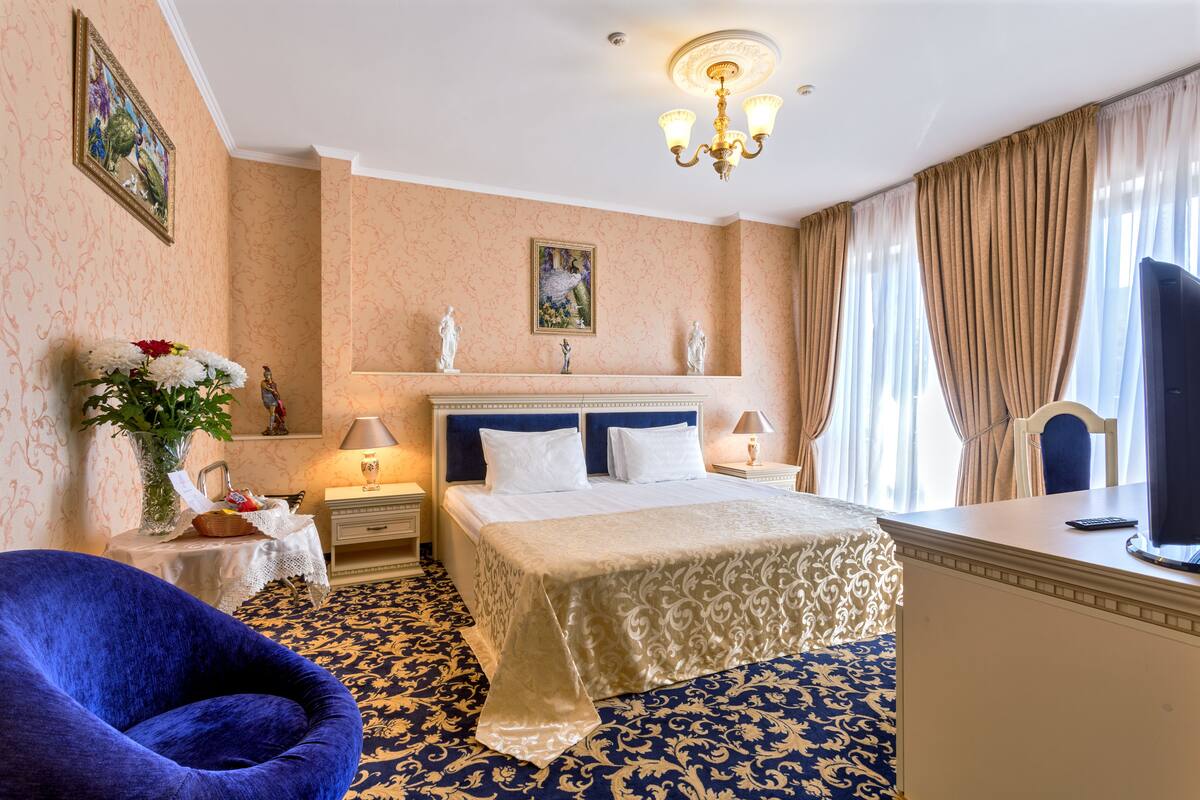Hotellihuone, jossa on suuri sänky, työpöytä tietokoneella, sininen tuoli ja kattokruunu.