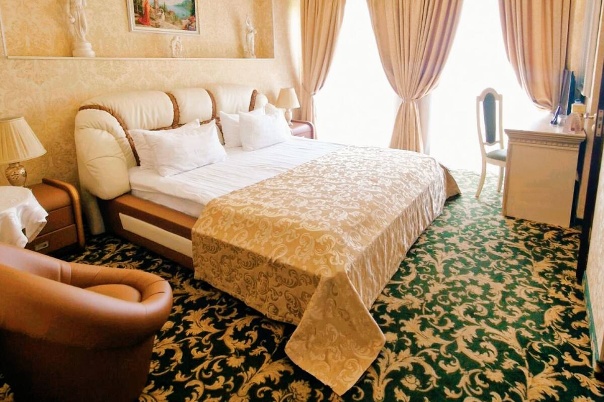 Hotellihuone, jossa on suuri sänky, työpöytä, tuoli ja matolla peitetty lattia.