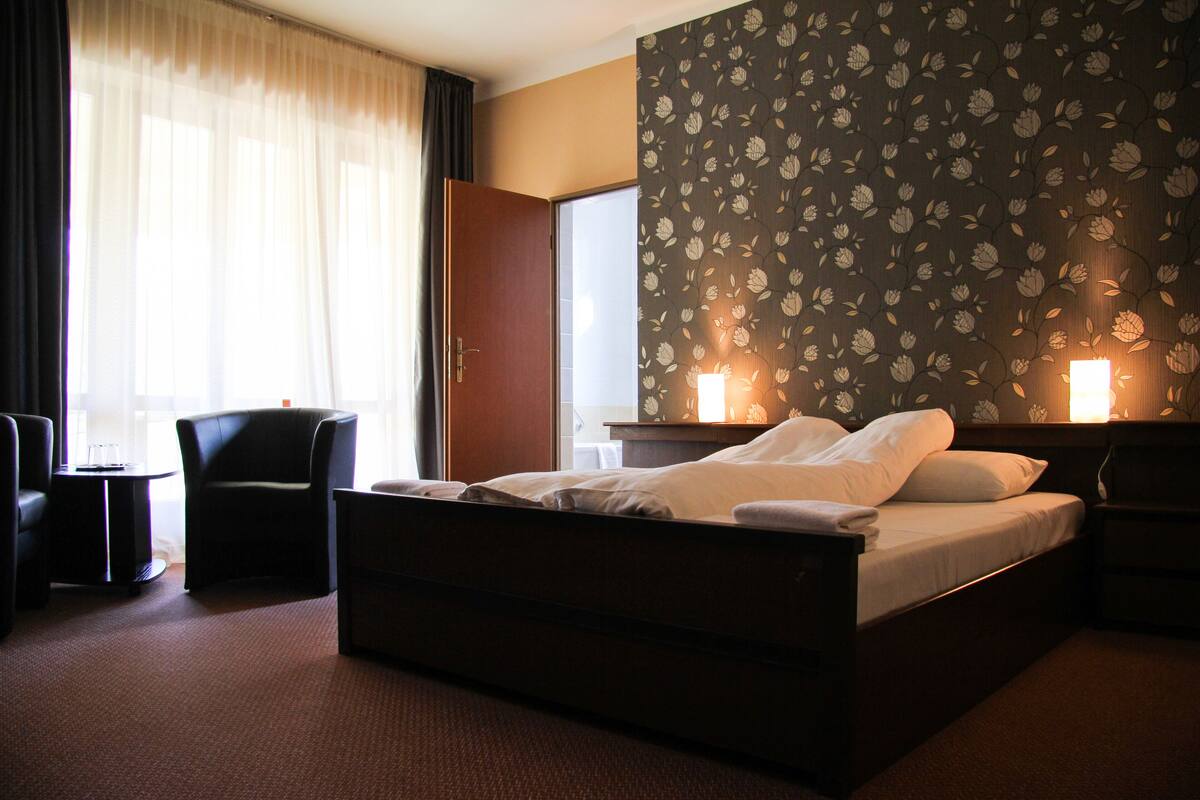 A hotel room with a bed, a chair, a desk, and a window with curtains.