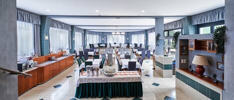 Un hall de hotel espacioso con zona de comedor central, varios conjuntos de asientos y una escalera que lleva a un nivel superior.