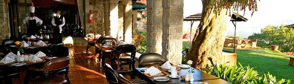 An outdoor restaurant with stone pillars, leather seating, and a view of the sea.