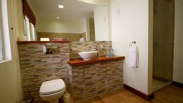 A modern bathroom with a stone backsplash, a white toilet, a sink with a mirror above, and a shower area.