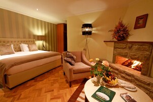 Habitación de hotel con una cama grande, un sofá, una chimenea y una mesa con libros y flores.