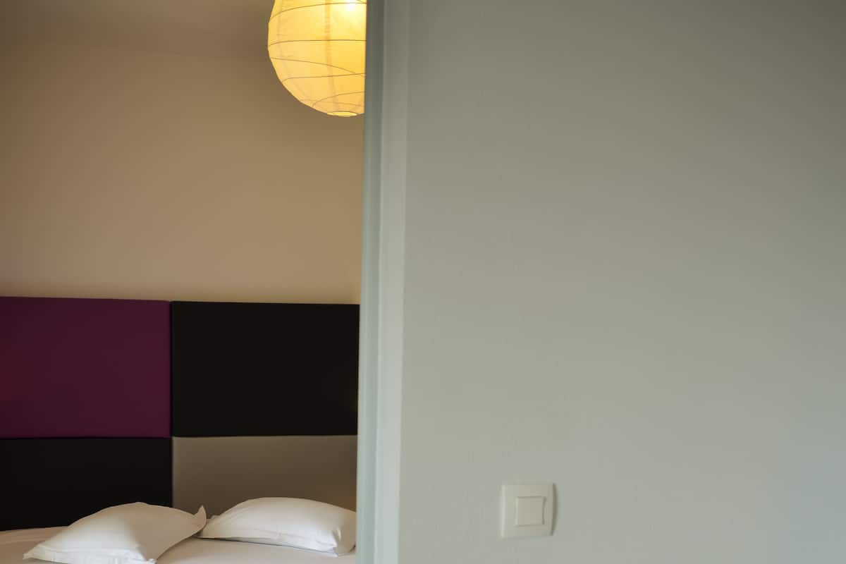 Quarto com cama, cadeira e luminária fixada na parede.