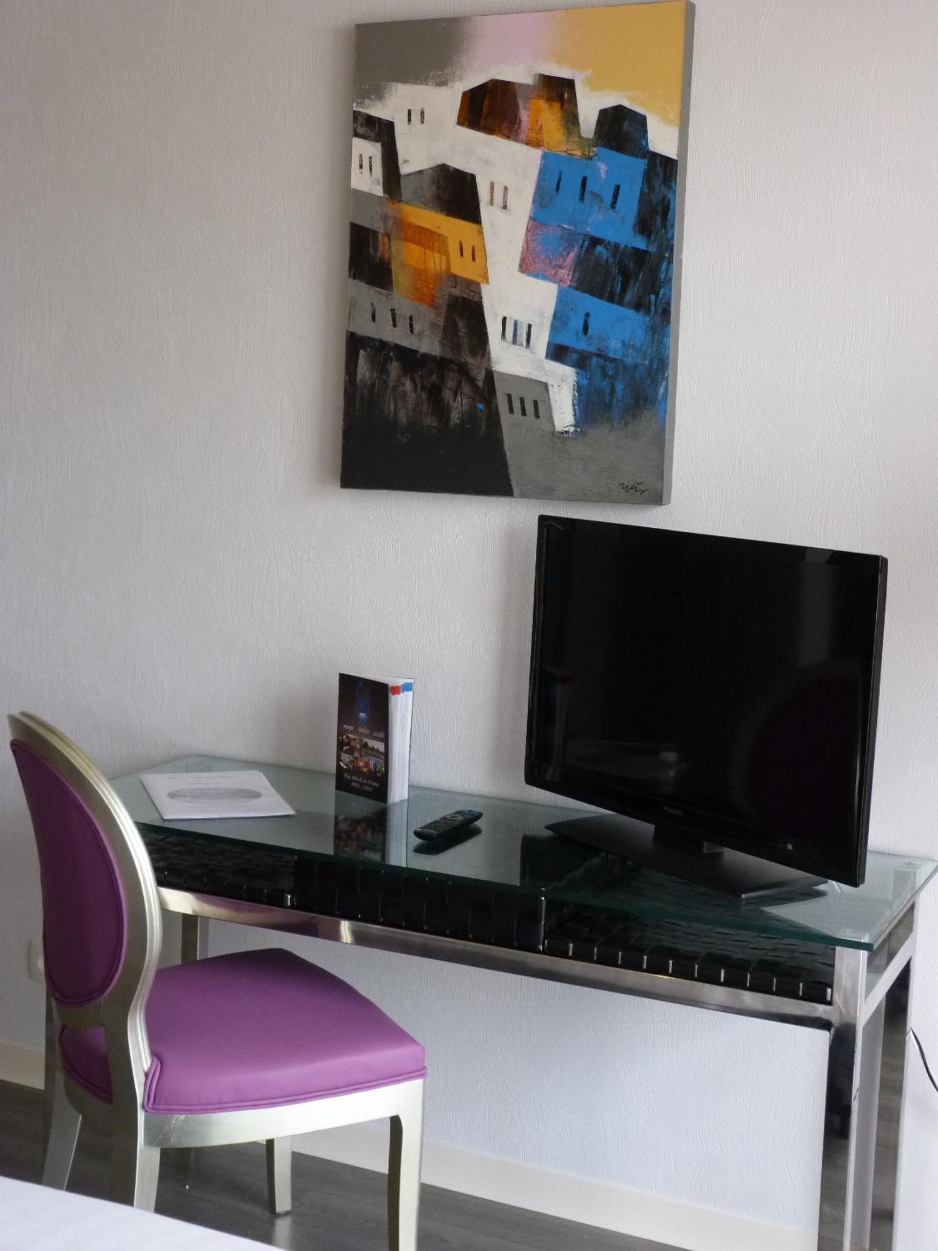 Ein modernes Zimmer mit einem Glastisch, einem violetten Sessel, einem Flachbildfernseher und einem farbenfrohen, abstrakten Gemälde an der Wand.