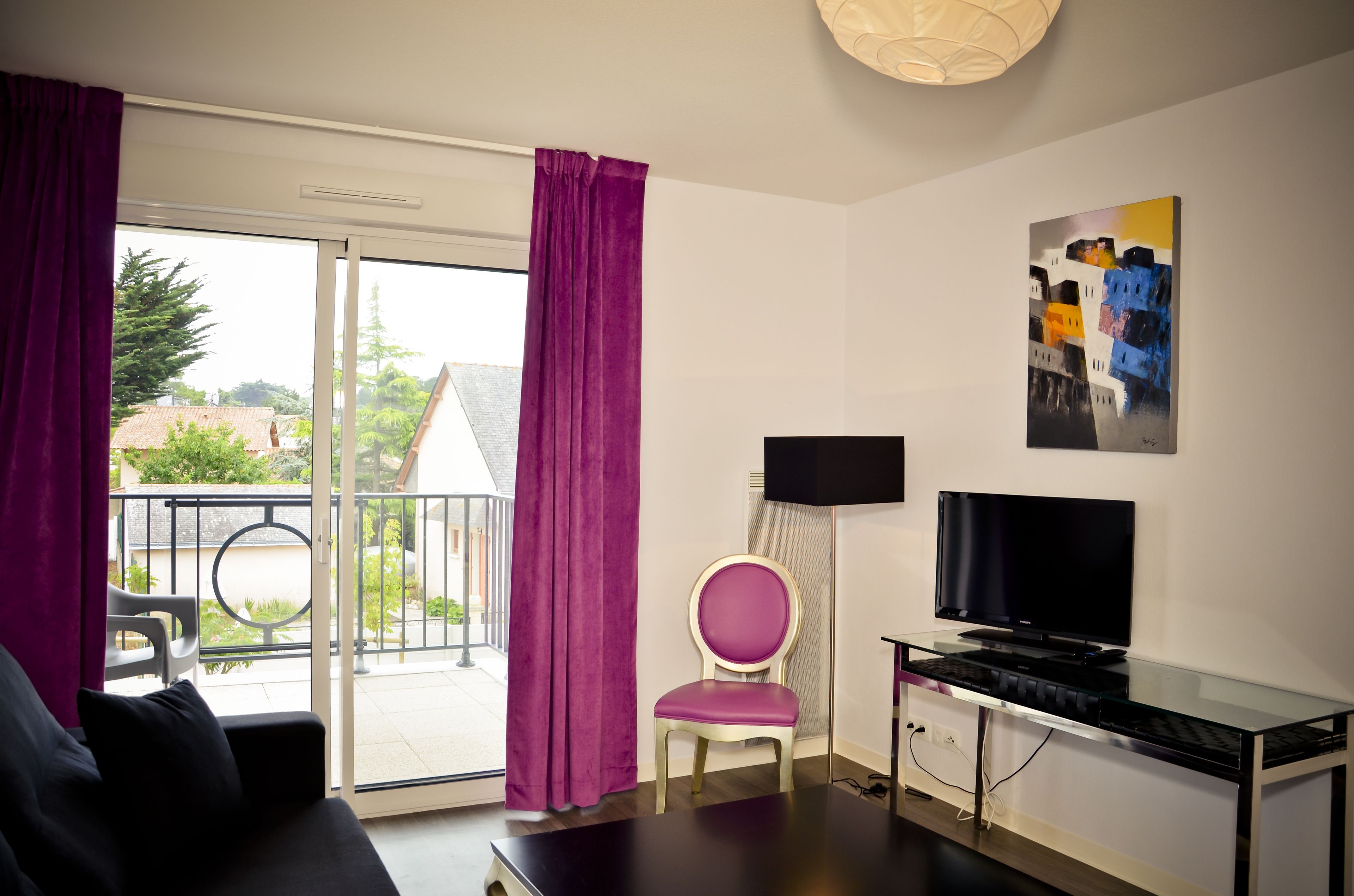 A modern room with a glass door leading to a balcony, a flat-screen TV, a small table, and a chair.