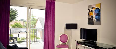 A modern room with a glass door leading to a balcony, a flat-screen TV, a small table, and a chair.