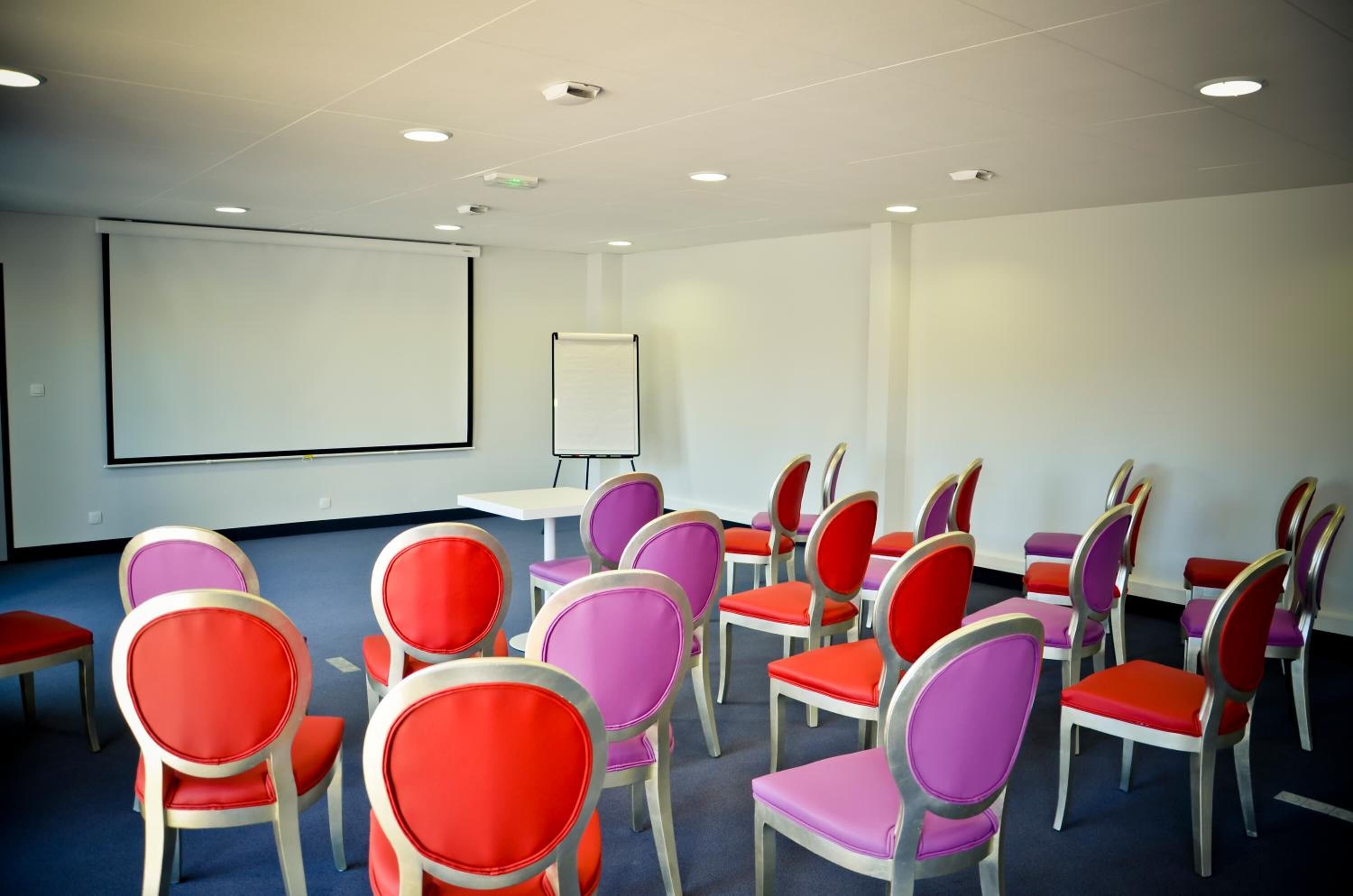 Uma sala de conferências com fileiras de cadeiras, um quadro branco e uma tela de projeção.